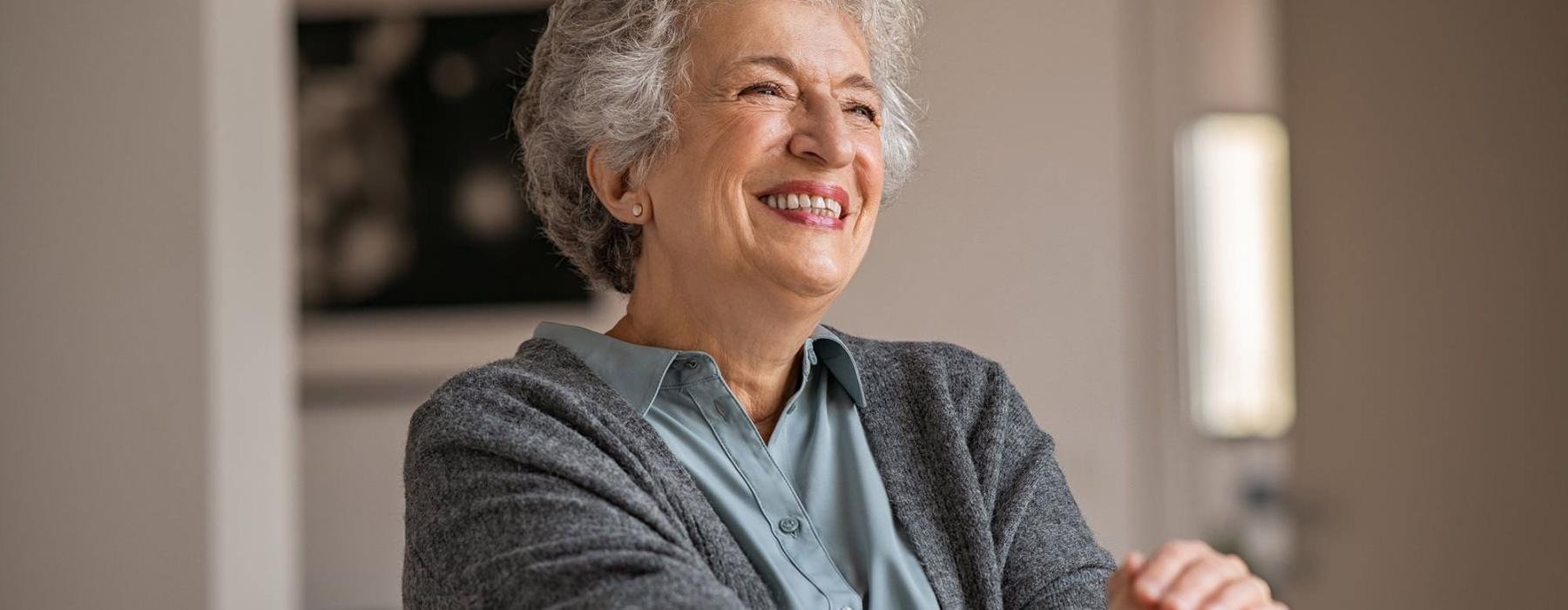 elderly woman with a cane, sits in a room and smiles